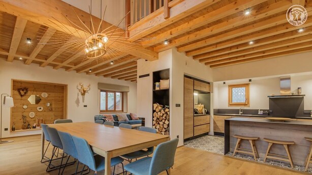Una cocina moderna con vigas de madera, una zona de comedor con sillas azules y una chimenea.