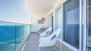 Een balkon met twee witte rieten stoelen, een ronde zithoek en uitzicht op de oceaan.