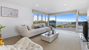 Uma sala de estar moderna com um sofá, uma mesa de centro e uma janela ampla com vista para o mar.