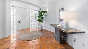 Interior moderno com parede branca curva, planta em vaso, tapete redondo e bancada de mármore com luminária.