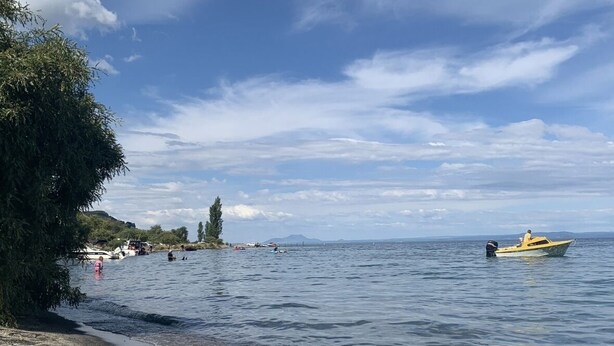 Una playa con aguas tranquilas, un bote y una costa lejana con edificios.