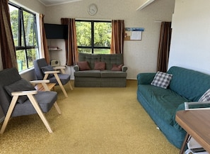A cozy living room with a grey sofa, a teal sofa, and a grey armchair. There is a small wooden table and a television mounted on the wall.