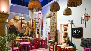 Un restaurante con mesas y sillas rojas, cestas colgantes y un letrero de NV Opticas.