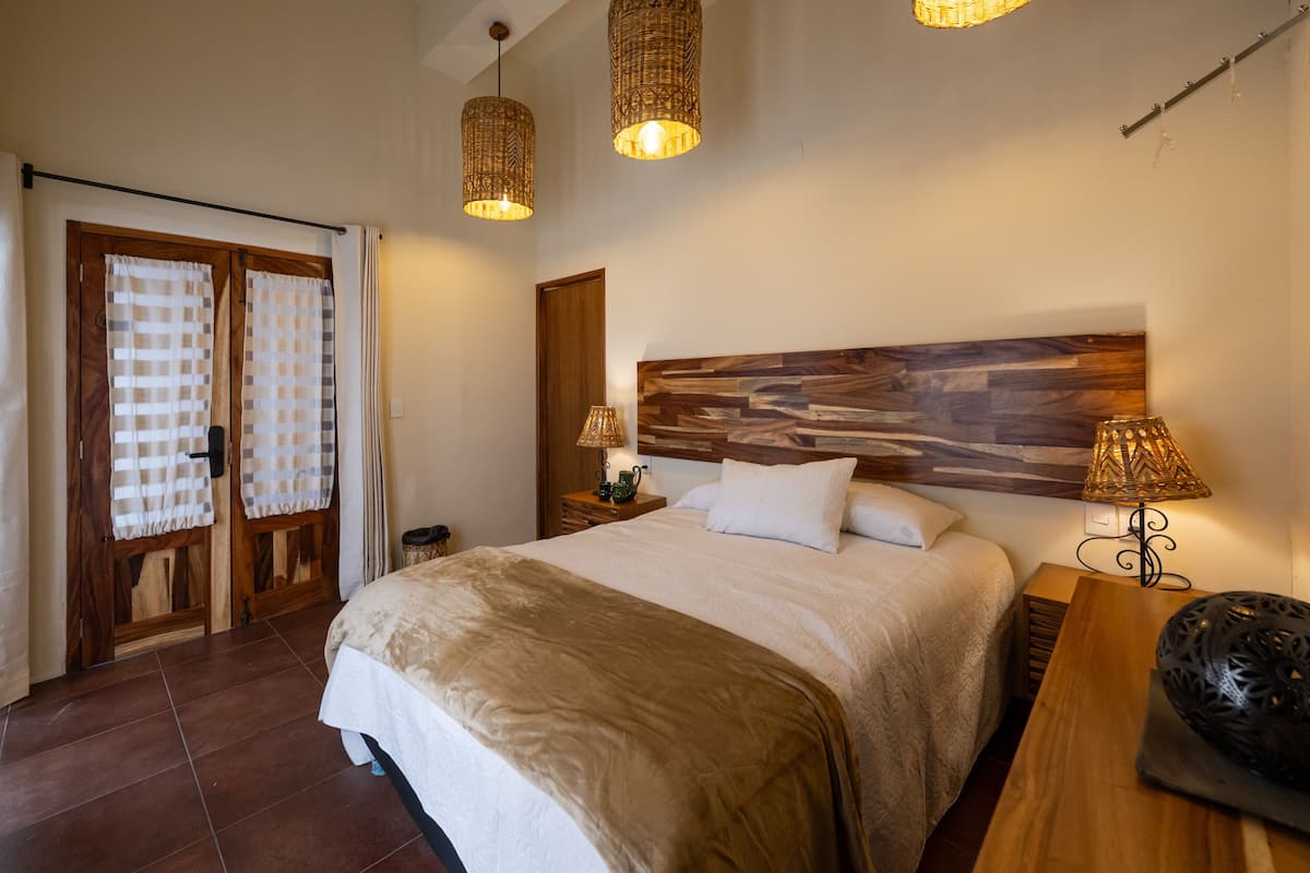 Un dormitorio con una cama grande, cabecera de madera, dos lámparas de noche y un mesita de noche de madera.