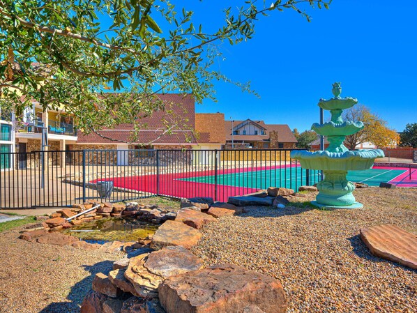 A tennis court with a fountain, surrounded by a fence and pebbles.