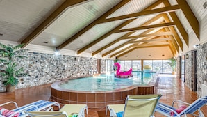 En indendørs swimmingpool med stenvæg, træbjælker og liggestole.