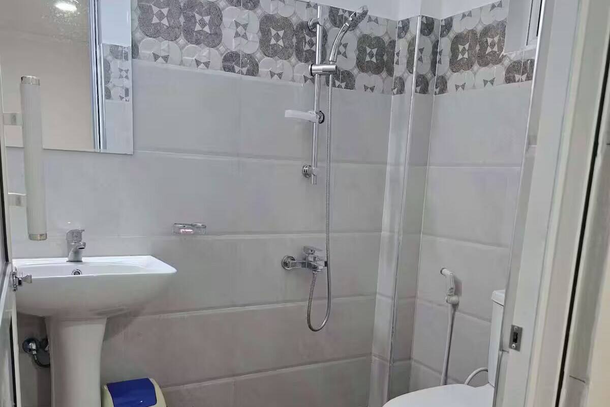 A bathroom with a white sink, a toilet, and a shower. The floor has a patterned tile design.