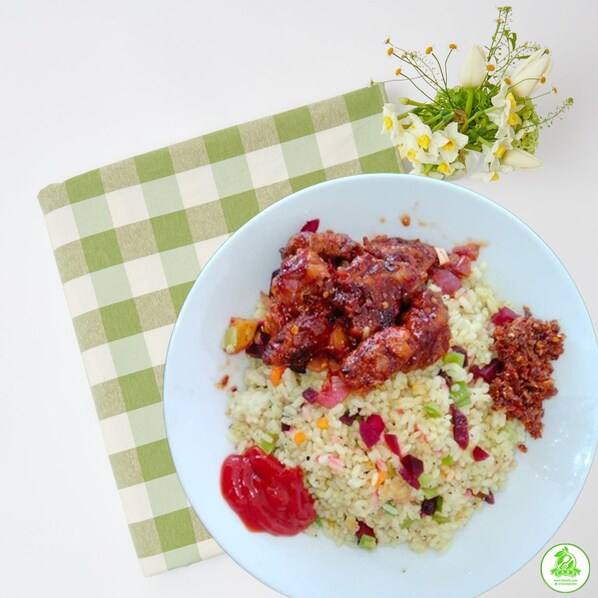 A plate of food with rice, vegetables, and a meat dish, accompanied by a green and white checkered napkin and a small bouquet of flowers.