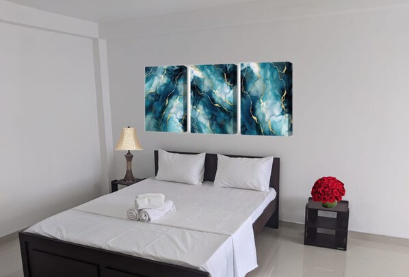 A neatly made bed with white linens, a bedside lamp, and a floral arrangement on a nightstand. - MPM Apartment -Manawickrama Building  (Kandy)