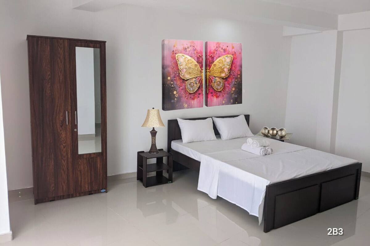 A modern bedroom with a bed, a nightstand, a lamp, a wardrobe, and two butterfly paintings on the wall.