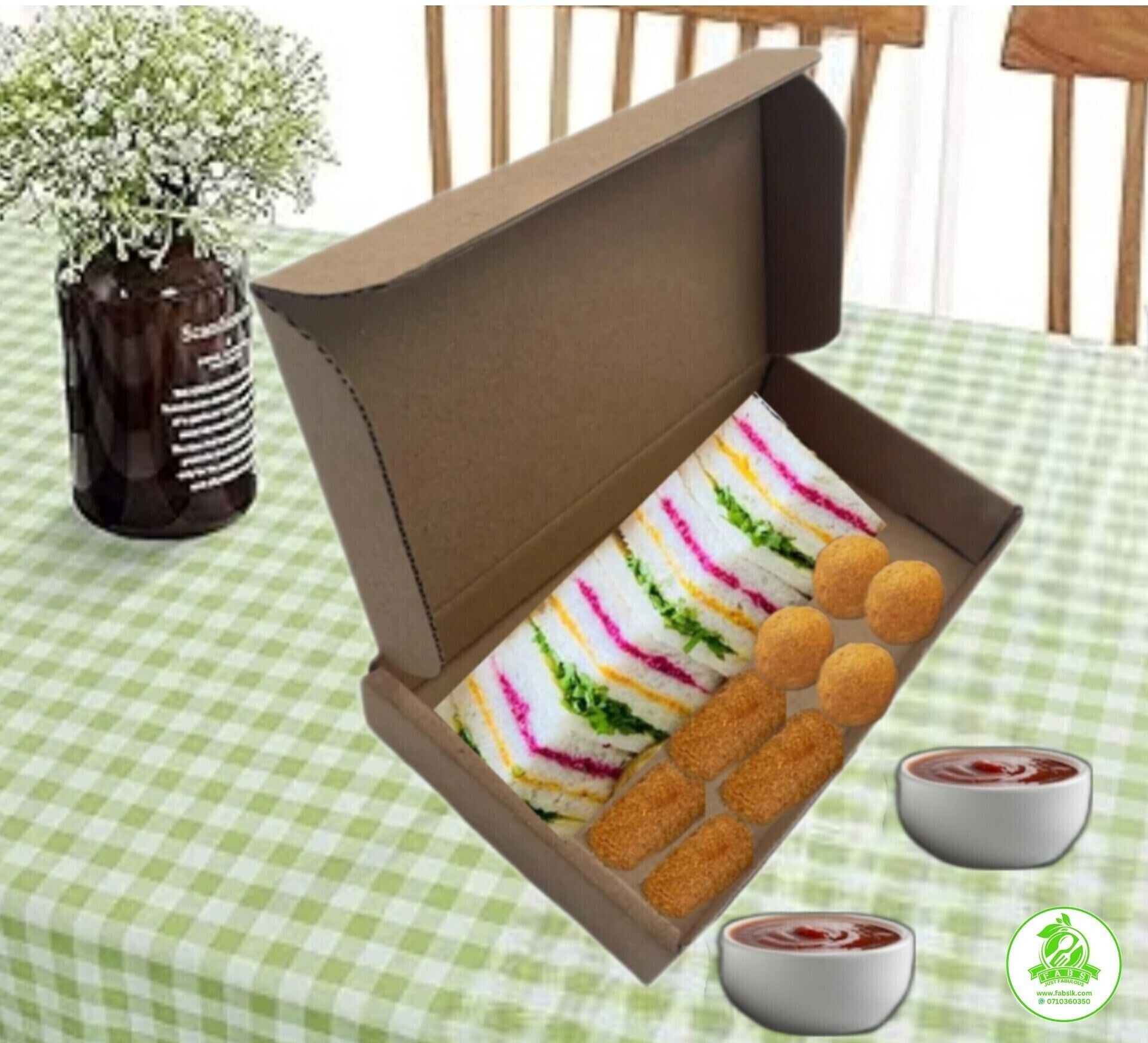 A table with a checkered tablecloth, a brown box containing sandwiches and croquettes, and two small bowls of sauce.