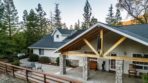 A house with a covered patio, stone pillars, and a wooden deck. - Scenic Mountain Views w/ Game Room, Pool & Hottubs (Oakhurst)
