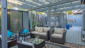 A covered patio area with wicker furniture, a glass coffee table, and a patterned rug.