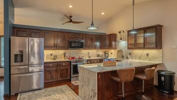 A modern kitchen with dark wooden cabinets, stainless steel appliances, a large island with bar stools, and pendant lighting.