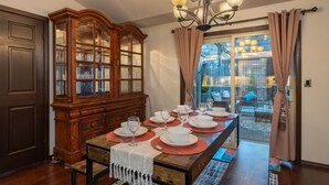 A dining room with a wooden dining table set for six, flanked by a glass-fronted china cabinet and a dark wooden door.