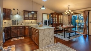 A spacious kitchen with dark wood cabinets, a marble island, and pendant lighting.