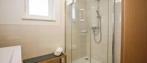 Une salle de bain moderne avec une douche à parois de verre, un banc en bois et un lavabo blanc.