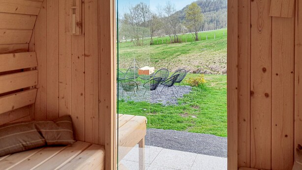 A wooden cabin with a glass door leading to an outdoor seating area with chairs and a table.