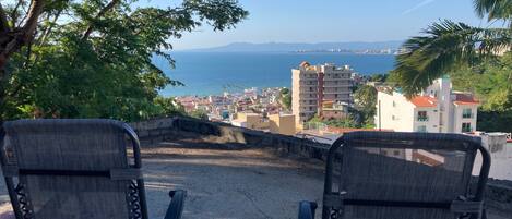 Two chairs facing a scenic view of a coastal town with buildings and a clear sky.