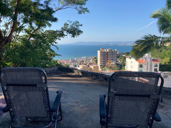 Due sedie rivolte verso una vista panoramica di una cittadina costiera con edifici e cielo sereno.