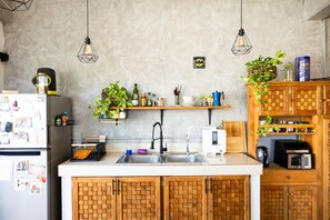 A kitchen with wooden cabinets, a stainless steel sink, hanging pendant lights, and various kitchen appliances.