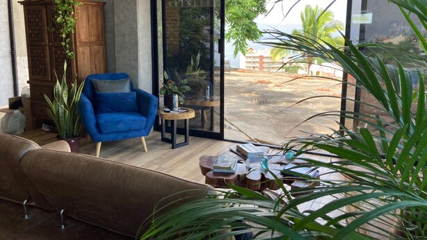 Un salon moderne avec un fauteuil bleu, un meuble en bois et une grande fenêtre donnant sur un immeuble et des arbres.