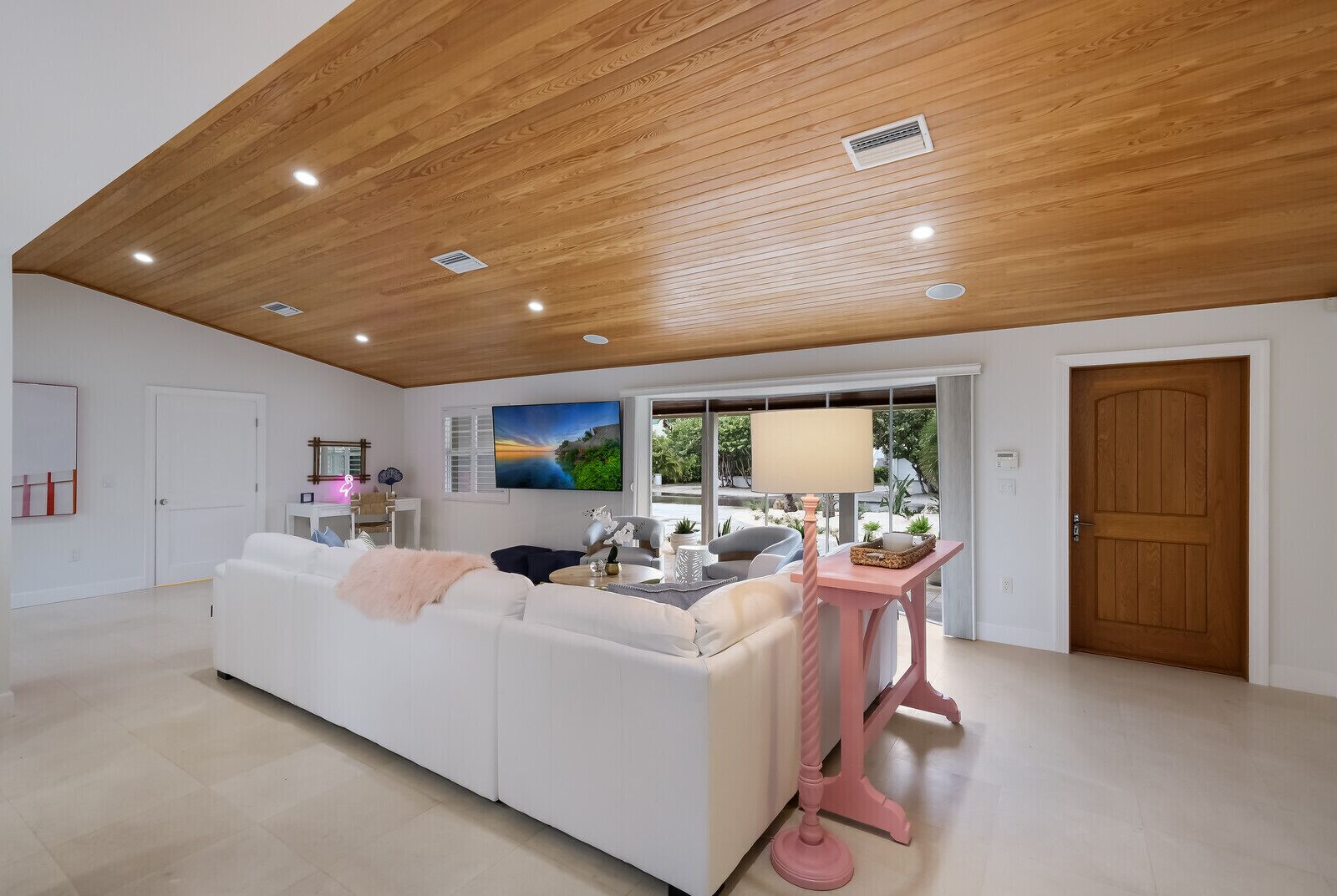 Ein geräumiges Wohnzimmer mit einem weißen Sofa, einem rosafarbenen Tisch und einer Holzbalkendecke.