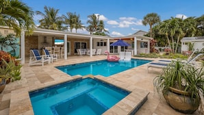 A pool area with two separate pools, lounge chairs, and a pink flamingo float. - Canal Walk: Tiki Bar, Mini Golf, Pool & Spa On Canal by Anna Maria Life Vacation Rentals (Anna Maria)