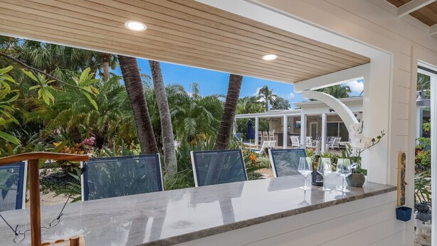 An outdoor dining area with a view of a pool and palm trees. - Canal Walk: Tiki Bar, Mini Golf, Pool & Spa On Canal by Anna Maria Life Vacation Rentals (Anna Maria)