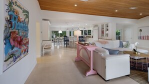 A spacious living area with a wooden ceiling, white furniture, and a large painting on the wall. - Canal Walk: Tiki Bar, Mini Golf, Pool & Spa On Canal by Anna Maria Life Vacation Rentals (Anna Maria)