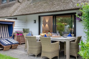 Eine Terrasse mit Korbmöbeln, einem Tisch mit Gläsern und einer Schale, sowie einer reetgedeckten Struktur.