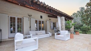 Une terrasse extérieure avec des meubles blancs, notamment des canapés et des fauteuils, et un mur en pierre agrémenté de fenêtres.