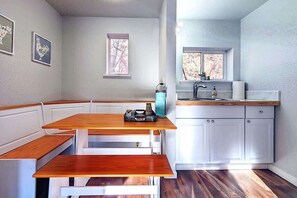 A kitchen with a wooden table and bench, white cabinets, a window, and a sink.