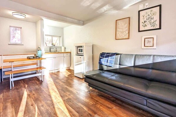 A living room with a black leather sofa, wooden bench, and a kitchen in the background.