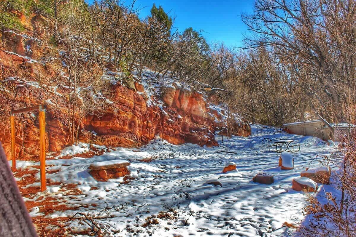 A snowy outdoor area with a rocky hillside, wooden fence, and a bench.