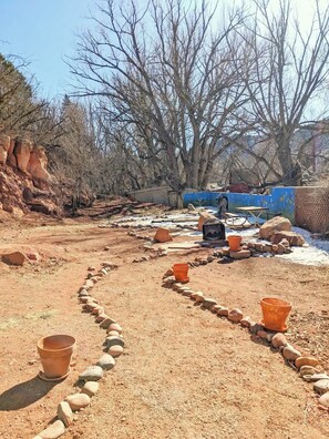 A garden with a stone pathway, terracotta pots, and a blue wall.