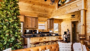 Een gezellig chalet interieur met houten details, een kerstboom, een leren bank en een keukenhoek.