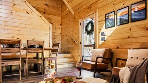 Een gezellig houten blokhut interieur met een eethoek, houten stoelen, een open haard en uitzicht op de natuur.