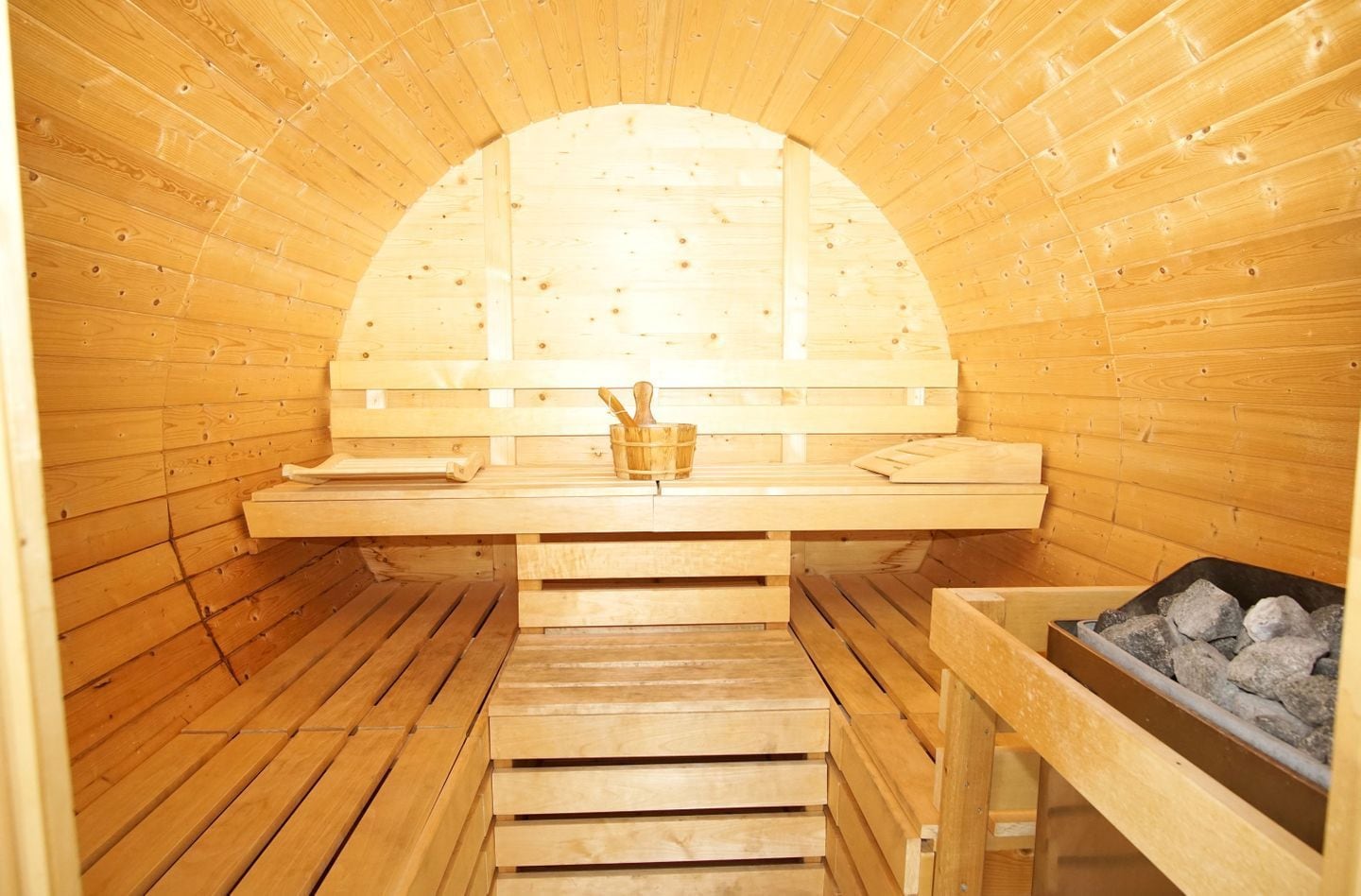 A sauna with wooden benches, a wooden bench with a bucket, and a container of stones.
