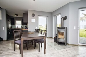 Une cuisine moderne avec des meubles de couleur sombre, un coin repas avec une table et des chaises en bois, et un poêle à bois.