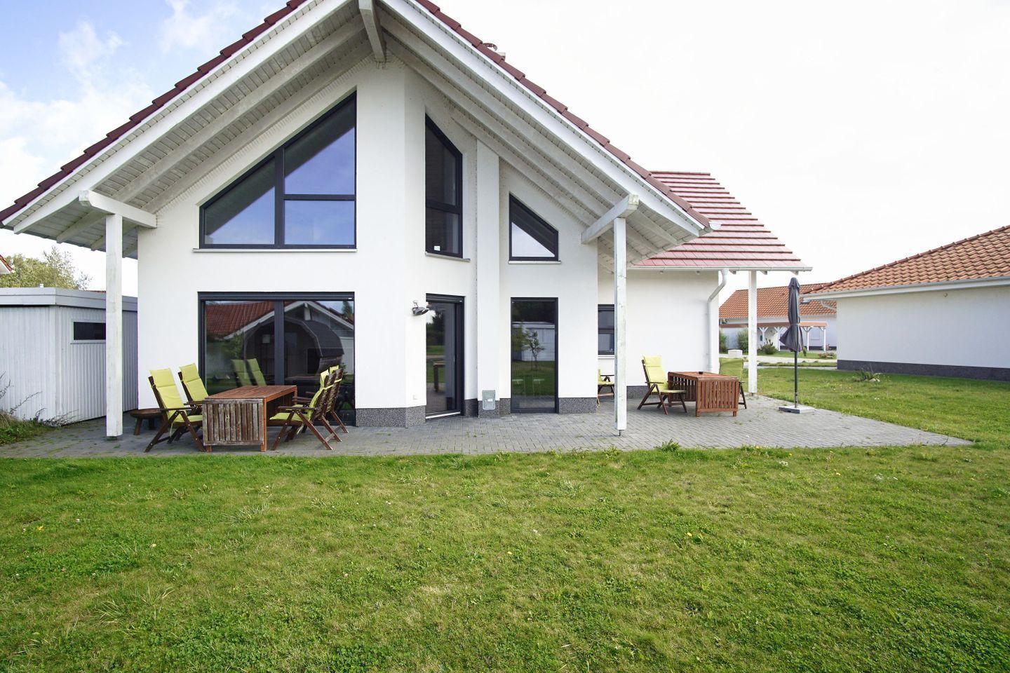 A modern two-story house with a covered patio, large windows, and a barbecue area.