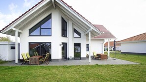 Ein modernes, zweistöckiges Haus mit überdachter Terrasse, großen Fenstern und Grillplatz.