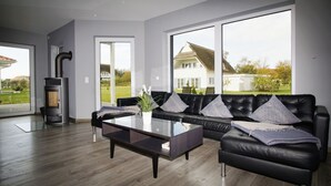 Ein modernes Wohnzimmer mit einem schwarzen Ledersofa, einem Glastisch und einem Kaminofen.