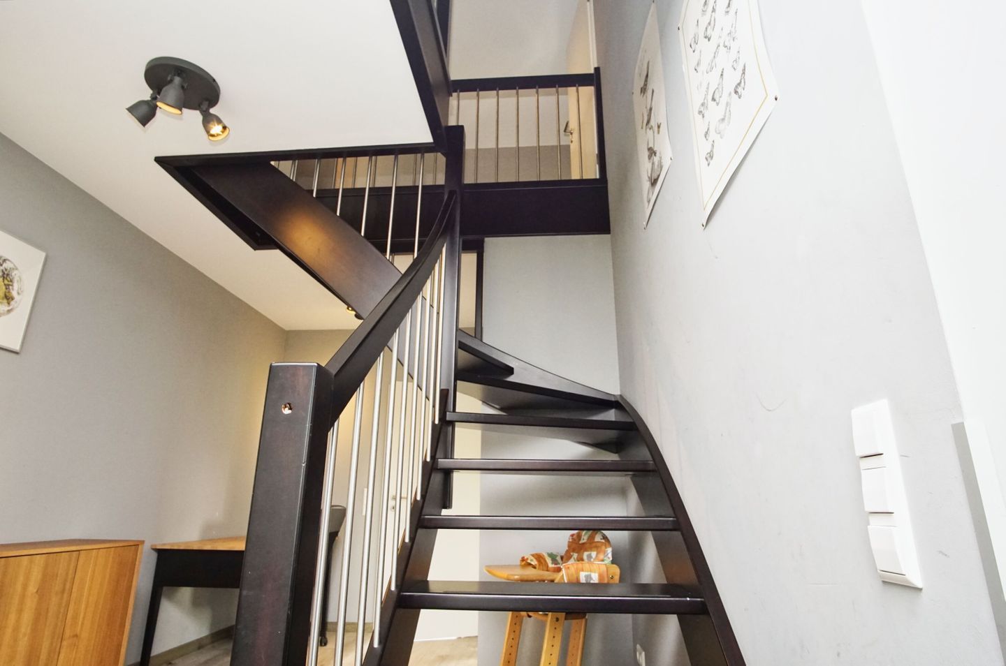 A modern staircase with a dark metal railing and a light fixture above.