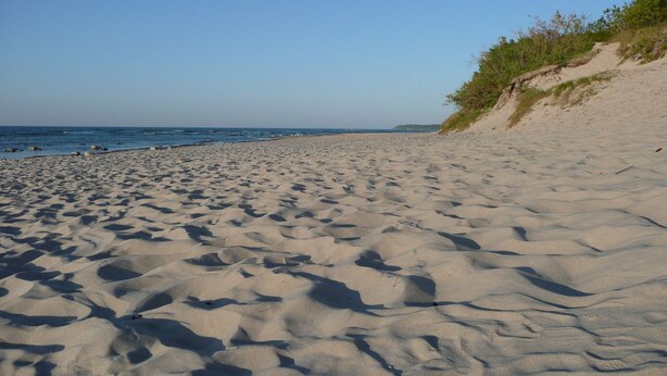 Ein sandiger Strand mit sanften Wellen und blauem Himmel.