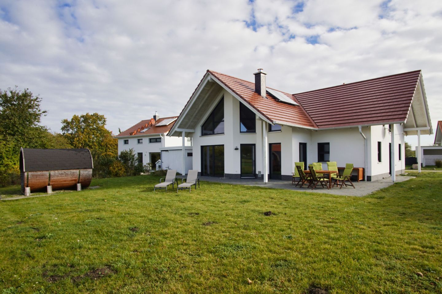 A modern two-story house with a sloped roof, a covered patio, and a barrel-shaped structure in the yard.
