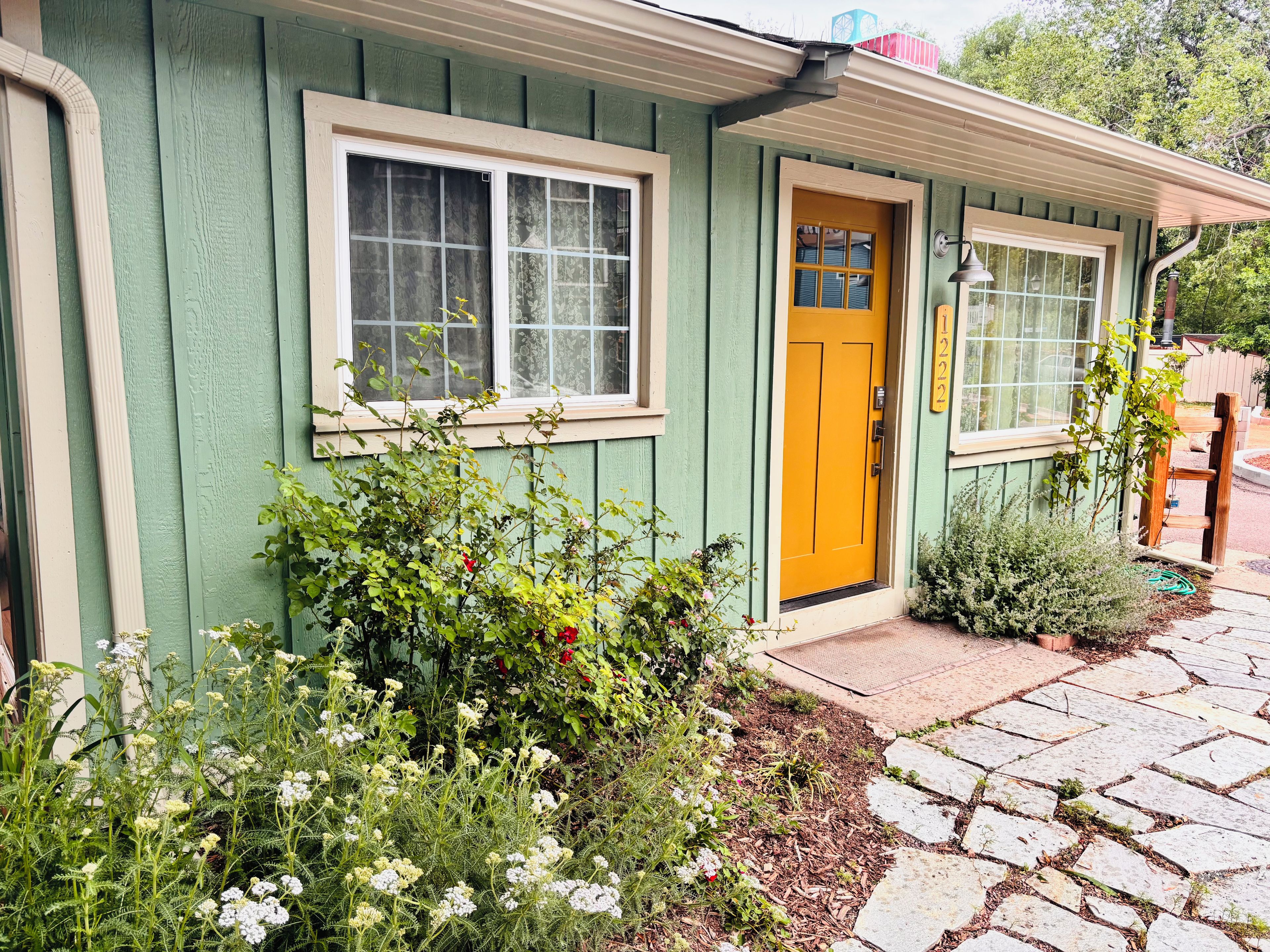 Une maison à l’extérieur vert, avec une porte jaune et une fenêtre dotée d’un cadre blanc.