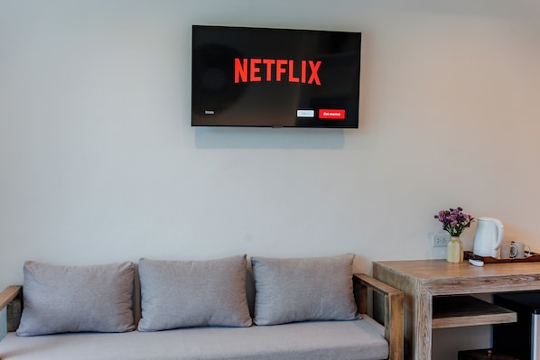 A living room with a television displaying the Netflix logo, a sofa, and a wooden side table with a vase and a coffee maker. - LOVE Beach Club (Koh Samui)