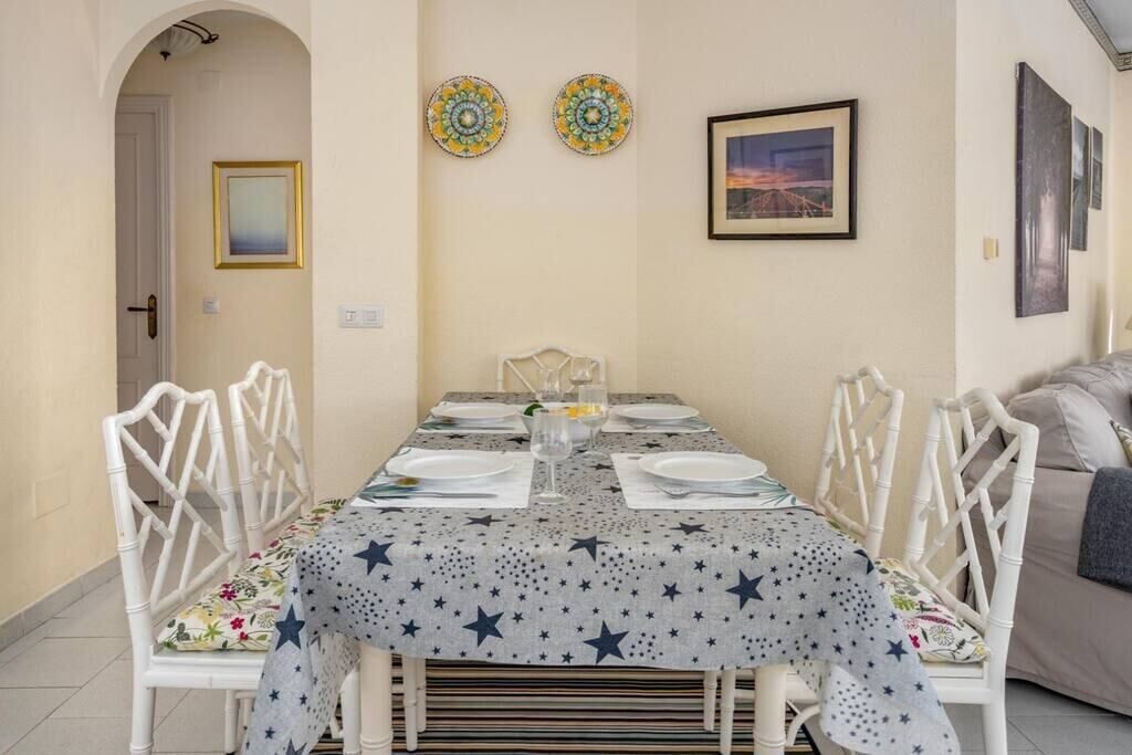 A dining area with a table set for four, white chairs, a star-patterned tablecloth, and decorative plates on the wall.