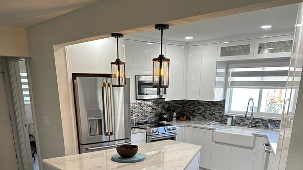 Una cocina moderna con una isla grande, suelo de madera oscura, armarios blancos e iluminación colgante.